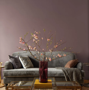 Paint 2025 Color of the Year from Benjamin Moore. A purple-brown wall with a gray couch and coffee table with a tree on it.
